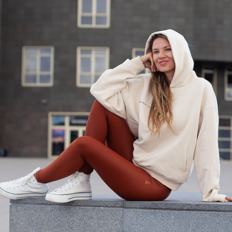 Sitzende Frau mit Hoodie und INASKA Leggings in Rostbraun