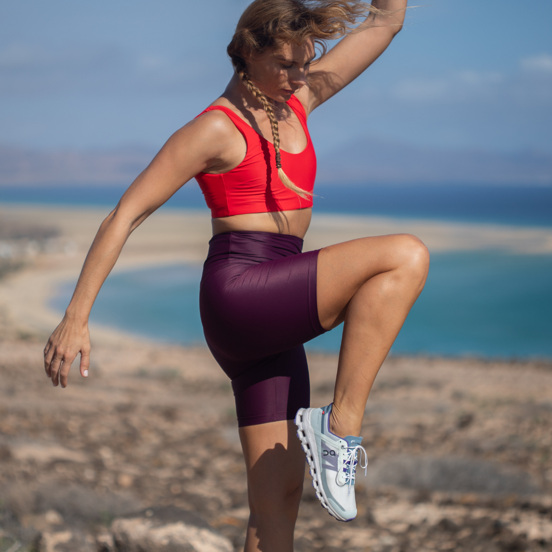 Frau mit nach oben gerichteten Knie trägt INASKA Radler Hose in Berry am Strand